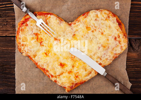 Pizza Margherita a forma di cuore con posate su un tavolo di legno, vista dall'alto. Culinario mangiare pizza. Foto Stock