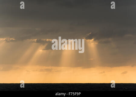 Sunrise cloudscape con luce arancione e raggi del sole da dietro le nuvole pesanti Foto Stock