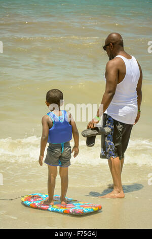 Vista posteriore di African American boy di indossare un giubbotto salvagente con il suo boogie board e un adulto americano africano uomo al litorale Foto Stock