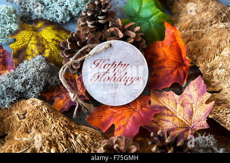 'Happy Holidays' scritto sul tag di legno con foglie e pigne nelle quali Foto Stock