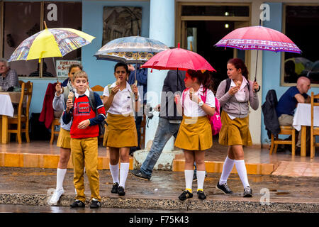 Gli scolari, studenti attraversare una strada in Vinales, pioggia, ombrelli, mangiare il gelato, Viñales, Cuba, Pinar del Rio, Cuba Street Foto Stock