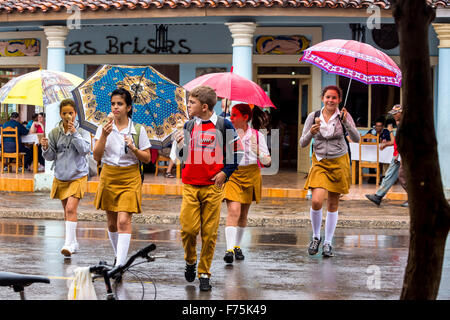 Gli scolari, studenti attraversare una strada in Vinales, pioggia, ombrelli, mangiare il gelato, Viñales, Cuba, Pinar del Rio, Cuba Street Foto Stock