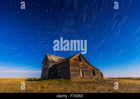 Stella circumpolare sentieri volteggiare al di sopra di un vecchio rustico e casa abbandonata vicino all isola di prua, Alberta, con illuminazione da ne Foto Stock