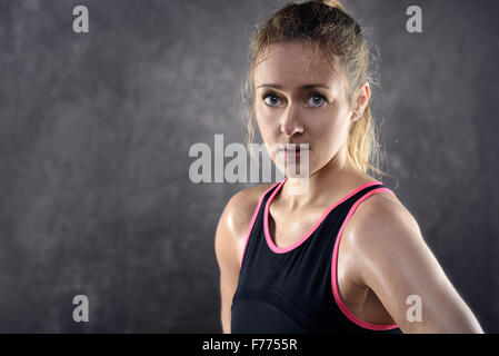 Testa e spalle il ritratto di una sudorazione Athletic donna bionda indossando rosa e nero serbatoio superiore e in piedi con le mani sui fianchi mi Foto Stock