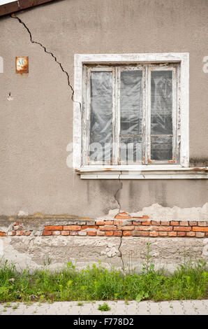 Casa decrepita parete incrinata e fessura, vecchia casa abbandonata con la lamina nella finestra e bocchetta a lancia in tutto il lato, casa danneggiata... Foto Stock