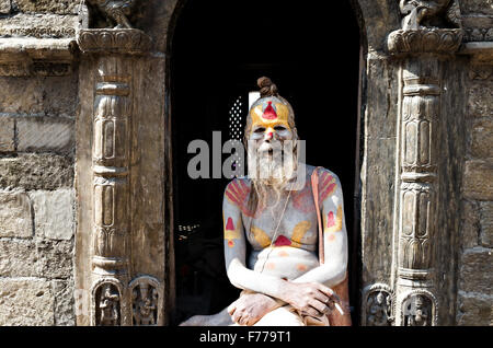 Un Sadhu indù (SAN) fumatori e sorridente al visualizzatore, tempio di Pashupatinath complessa, Kathmandu, 2015, il Nepal Foto Stock