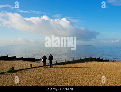 Coppia di mezza età che guarda al mare, Whitstable Beach, Kent, England Regno Unito Foto Stock