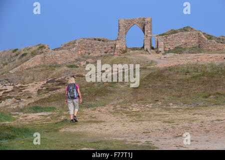 Lone Donna che cammina verso le rovine del XIV secolo il castello di Grosnez sulla maglia sentiero costiero. Foto Stock