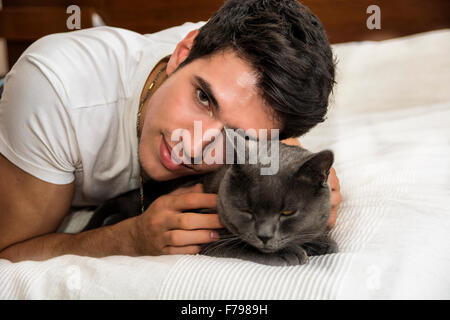 Bel giovane uomo Animal-Lover su un letto, avvolgente e coccole il suo grigio gatto domestico Pet. Foto Stock