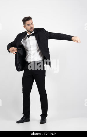 Giovane uomo mettendo sul vestito nero Tuxedo coat. Corpo pieno lunghezza ritratto su grigio di sfondo per studio Foto Stock