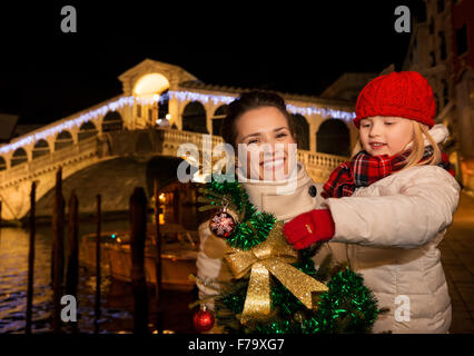 Famiglia moderna prendere il meglio della stagione di Natale da avente un affascinante viaggio a Venezia, Italia. Felice madre e figlia con albero di Natale nella parte anteriore del ponte di Rialto Foto Stock