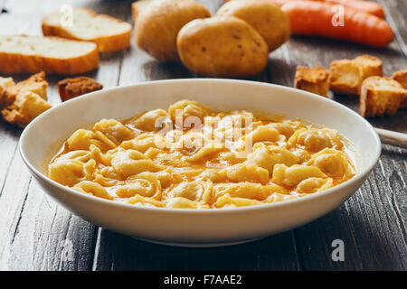 Zuppa di tortellini in piastra bianca sul tavolo di legno Foto Stock