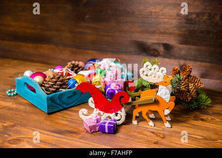 Vintage scatola di legno con decorazione di Natale, tinsel, pigne nelle quali, stelle, palline, slitta, la renna e doni su sfondo di legno, Foto Stock