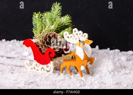 Composizione della decorazione di natale renne e Santa sleigh con ramo abete, pigne nelle quali le tracce nella neve su sfondo nero Foto Stock