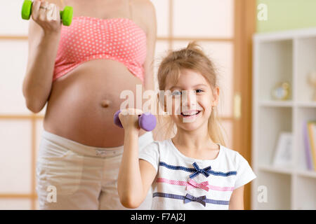 La donna incinta e il suo bambino più anziano facendo esercizi di fitness con manubri Foto Stock