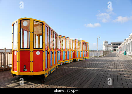 Una terra treno parcheggiato fino in corrispondenza di una estremità di un tradizionale molo sul mare a Weston-super-Mare, Regno Unito. Il treno è vivacemente colorato Foto Stock