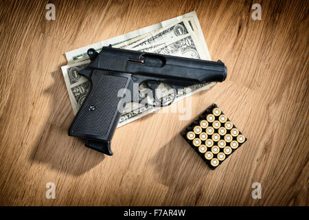Immagine di una pistola con cartucce e dollar note su un tavolo di legno Foto Stock