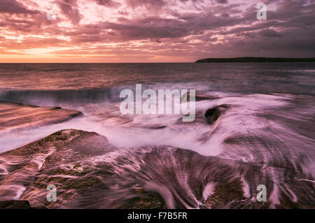 Sunrise seascape acqua con onde e piccola cascata di rocce in toni magenta a Sydney in Australia Foto Stock