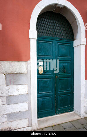 Una porta verde su una rosa con il muro di mattoni grigi Foto Stock