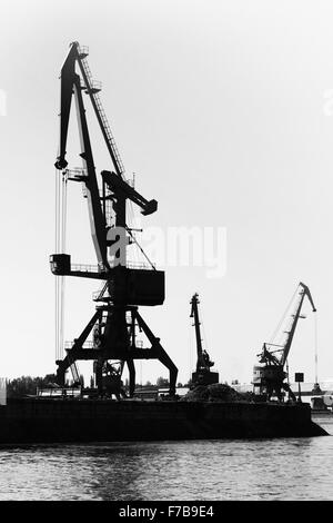 Sagome scure del porto industriale di gru. Danube River Coast in Bulgaria. In bianco e nero foto verticale Foto Stock