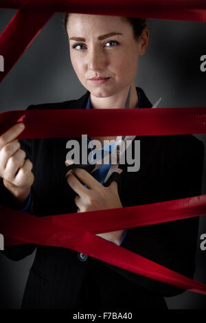 Business donna catturati dietro red di taglio del nastro il suo modo libero, girato in studio con bassa illuminazione tasto Foto Stock