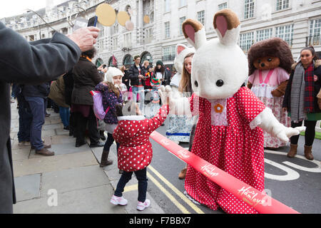 Londra, Regno Unito. Il 28 novembre 2015. Janhavi, 3 anni, dalla lettura interagisce con un carattere da famiglie di Sylvania. La cerimonia inaugurale di Natale Hamleys Toy Parade avviene lungo Regent Street, che andò e priva di traffico per il giorno. La sfilata organizzata dal famoso negozio di giocattoli Hamleys featured oltre 50 della nazione di figli prediletti di caratteri lungo con 400 animatori, una Marching Band e palloncini giganti. Il corteo è modellata su Macy's annuale di Thanksgiving Parade di New York. Credito: Immagini vibranti/Alamy Live News Foto Stock