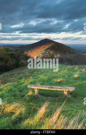 Una panca in legno sulla collina Jubillee accesa dal bel tramonto che è anche illuminazione di perseveranza Hill su Malvern Hills. Foto Stock