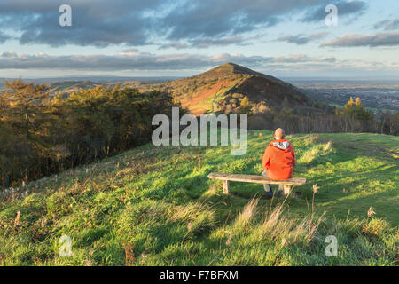 Un Walker in un arancio brillante rivestire si siede su una panca in legno sulla collina Jubillee per guardare il bellissimo tramonto che illumina la perseveranza Foto Stock