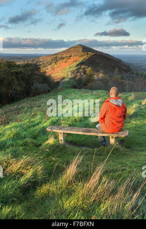 Un Walker in un arancio brillante rivestire si siede su una panca in legno sulla collina Jubillee per guardare il bellissimo tramonto. Foto Stock