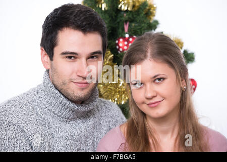 Coppia giovane, uomo e donna, seduti di fronte ad albero di natale Foto Stock