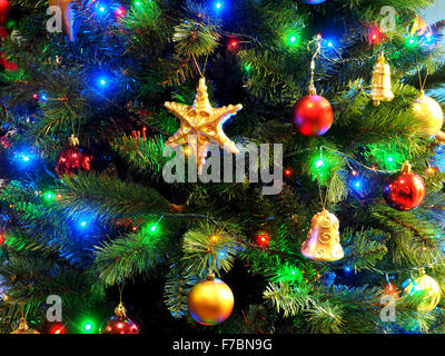 Colorato colorato display di luci festose e decorazioni su un albero di Natale artificiale con golden star campane e baubles Foto Stock