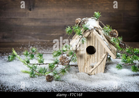 Birdhouse e albero di natale decorazione brunch nella neve su legno rustico sfondo. Foto Stock