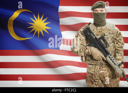 Soldier holding mitragliatrice con bandiera nazionale sullo sfondo - Malesia Foto Stock