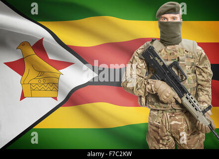 Soldier holding mitragliatrice con bandiera nazionale su sfondo - Zimbabwe Foto Stock