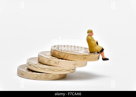 Femmina miniaturizzati pensionato seduto bilanciato su una pila di libbra di monete Foto Stock