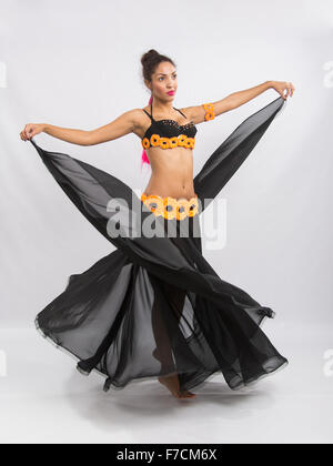 Ragazza giovane mulatto dancing in un lungo nero candido abito aperto, è isolato su uno sfondo luminoso Foto Stock