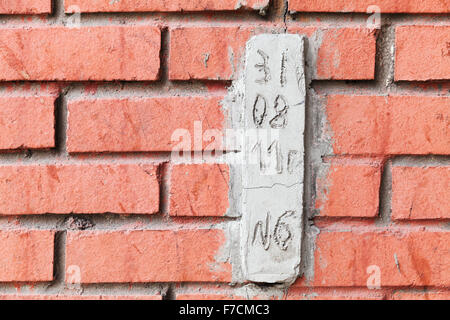 Speciale blocco di calcestruzzo con data di osservazione crepe in rosso e parete di mattoni Foto Stock