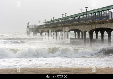 Le tempeste e grandi onde si infrangono in Boscombe Pier, Bournemouth Dorset, Regno Unito. Una persona che si trova alla fine del molo. Foto Stock