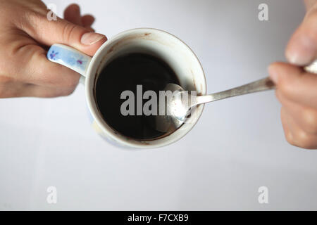 Una tazza di cucchiaio di caffè nero mattutino in mani femminili. Tazza di caffè dall'alto Foto Stock