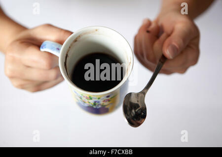 Una tazza di caffè nero mattutino in mani femminili. Tazza di caffè da sopra il cucchiaio Foto Stock