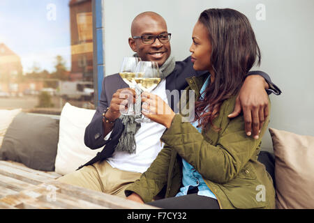 Felice giovane africano coppia americana godendo di un romantico un bicchiere di vino bianco come si siedono a braccetto in un ristorante Foto Stock