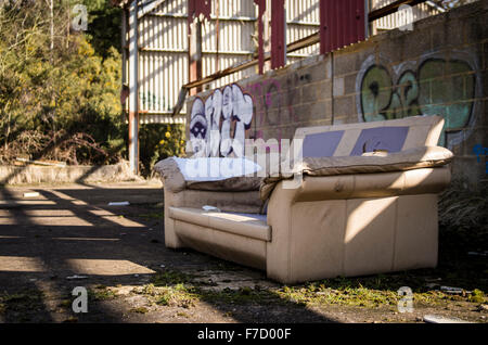 Un divano abbandonato davanti al coperto di graffiti a parete di un abbandonato edificio commerciale Foto Stock