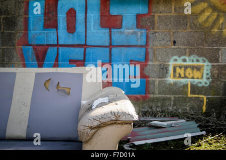 Un divano abbandonato davanti al coperto di graffiti a parete di un abbandonato edificio commerciale Foto Stock