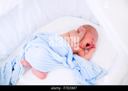 Neonato boy svegliarsi in una mattina di sole nel letto bianco. Nuovo nato figlio che dorme e stretching nel cesto di Mosè Foto Stock