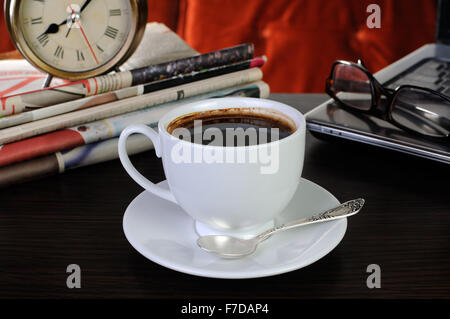 Tazza di caffè sul tavolo con quotidiani e il computer portatile Foto Stock