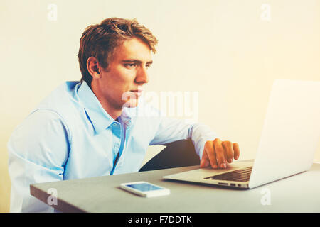 Giovane uomo Multitasking utilizzando laptop e Smart Phone che lavora da casa Foto Stock