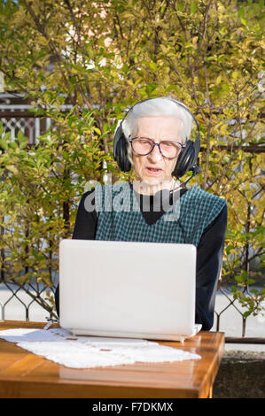 Senior donna avente una chiamata video su un notebook nel cortile posteriore usando le cuffie Foto Stock