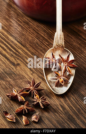 Anice stellato sul vecchio cucchiaio circondato da anice stellato su legno scuro tabella Foto Stock