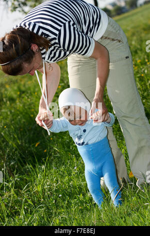 Un anno di età del bambino ad imparare a camminare da azienda di sua madre le mani Foto Stock