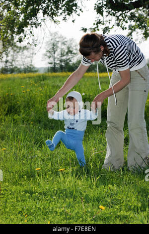 Un anno di età del bambino ad imparare a camminare da azienda di sua madre le mani Foto Stock